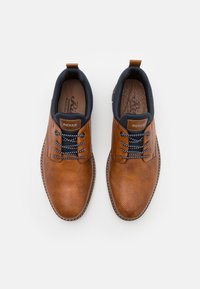 Chaussures en cuir marron à lacets avec une texture perforée, des accents bleu marine et des coutures blanches contrastantes autour de la semelle.