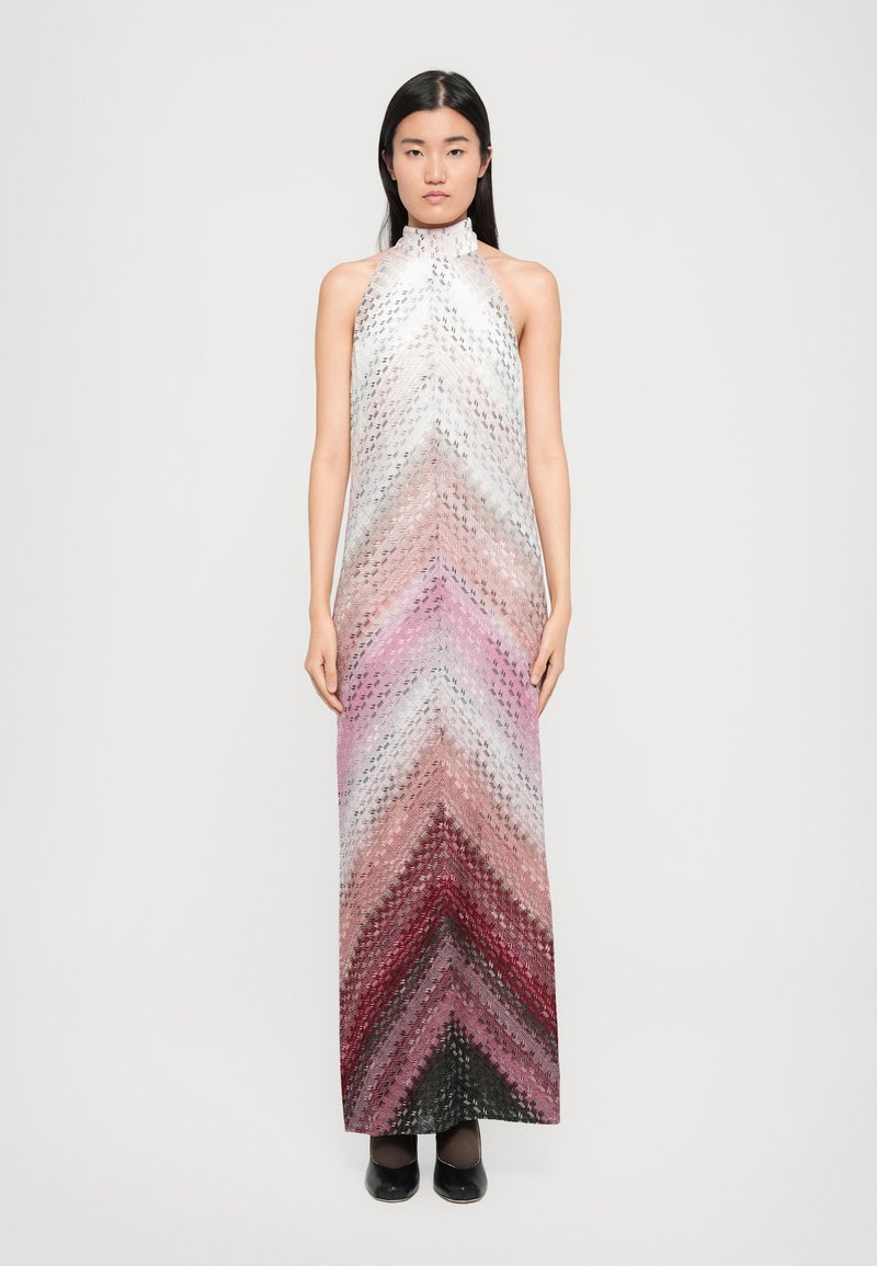 Naine seisab seistes, selg ees, kandes ilma varrukateta gradient halter-kleiti, millel on vihmapattern valge, roosa, punase ja mustaga, kombineerituna mustade kingadega.