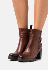 Bottes chelsea en cuir marron avec un talon carré, dotées d'une fermeture éclair latérale, de coutures horizontales et d'un panneau d'accent maroon.