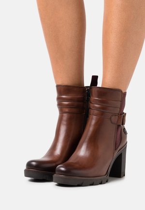 Botas de tobillo de cuero marrón con tacón cuadrado, que cuentan con una cremallera lateral, costuras horizontales y un panel de acento burdeos.