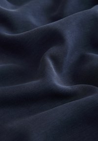 Mørk navyblåt stof med en glat tekstur, der har subtile bølger og en let glans, hvilket indikerer et let og fleksibelt materiale.