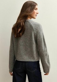 Grijze gebreide trui met lange mouwen en een ronde halslijn, met een zachte textuur en een crop-hem, gecombineerd met donker denim jeans.