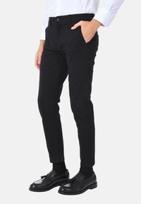 Pantaloni neri slim fit realizzati in tessuto resistente, caratterizzati da una linea affusolata, tasche laterali e una finitura liscia. Abbinati a mocassini neri.