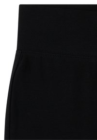 Gros plan sur la taille et les coutures d’un vêtement noir, montrant un tissu lisse et un détail de couture renforcée.