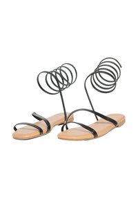 Sandali neri con cinturini a spirale alla caviglia, suola piatta beige, design minimalista, realizzati in materiali sintetici, con texture liscia.