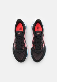Zwarte sport sneakers met roze strepen, ademend mesh bovenwerk, zwarte veters, gewatteerde kraag en witte buitenzool met blauwe accenten.