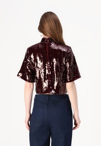 Burgundi säbriga lühikeste varrukatega crop top, kõrge kraega ja taga lukuga, koos kõrge vöökohaga tumedate denimipükstega.