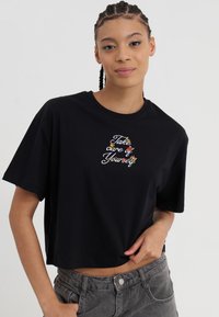 Black cropped t-shirt in soft fabric featuring colorful embroidered text “Take care of Yourself” at the center. Short sleeves and round neckline.