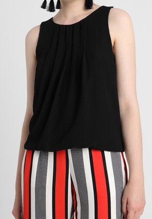 Sort ærmeløs top med frontplisseringer, båret med høj talje bukser med lodrette røde, sorte og hvide striber.