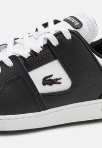 Zapatilla negra de cuero con detalles en blanco, paneles texturizados y logotipo. Presenta cordones blancos y una suela de goma para mayor agarre.