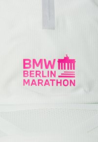 Hvitt stoff med ribbet tekstur som har en klar rosa grafikk som leser "BMW BERLIN MARATHON" og et bilde av Brandenburg-porten.