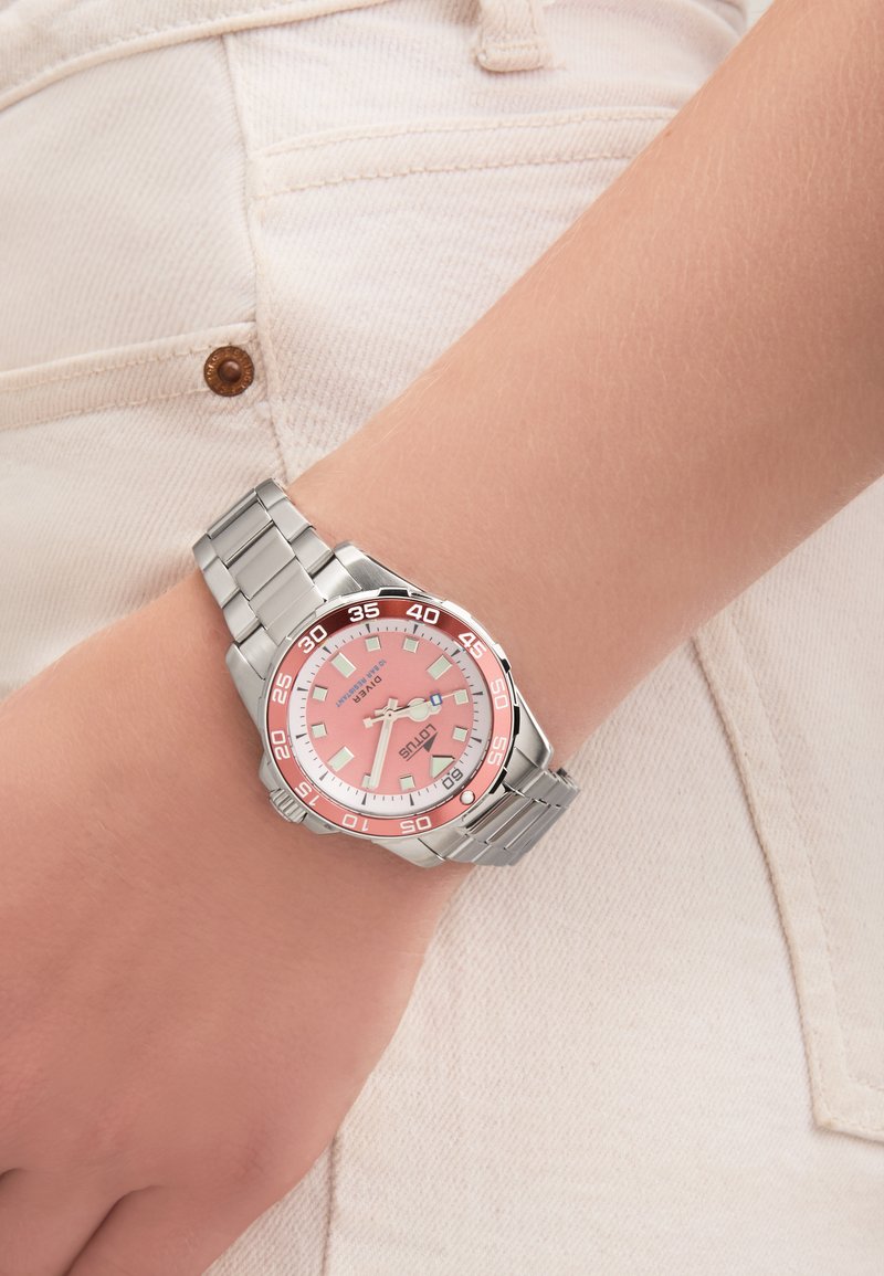 Armbandsur i rostfritt stål med en rosa urtavla, silverfärgade timmarkeringar och en röd bezel. Har armband av metall och en rund kasedesign.