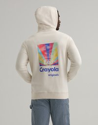 Hettegenser i beige stoff med en fargerik vintage Crayola-logo på baksiden, omgitt av stråler og tekst.