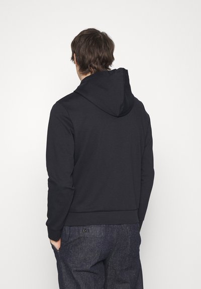 Black hoodie made of a soft, stretchy fabric with a relaxed fit. Features a drawstring hood and ribbed cuffs. Worn with dark denim pants.
