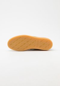 Semelle de chaussure avec une surface en caoutchouc orange lisse, présentant un motif en losange et un logo de la marque en relief au centre. Design propre et minimaliste.