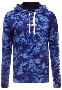 Sweat à capuche bleu tie-dye avec une poche kangourou, des cordons blancs et le logo "Hollister" à l'avant. Matière en polaire douce.