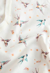 Fehér szövet kis színes fecskékkel repülés közben, szétszórt narancssárga csillag alakú és virágmotívumokkal.