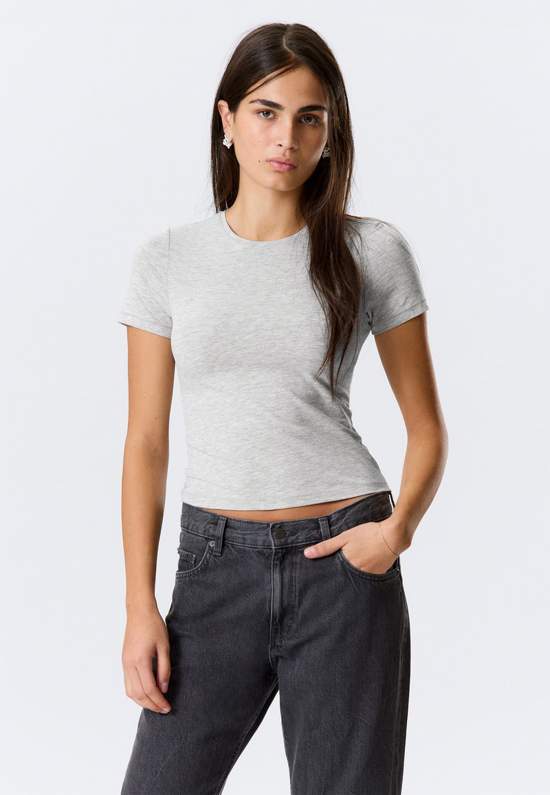 Graues kurzärmliges T-Shirt aus leichtem Baumwollstoff, taillierter Schnitt, runder Halsausschnitt, getragen mit hochtaillierten schwarzen Jeans.