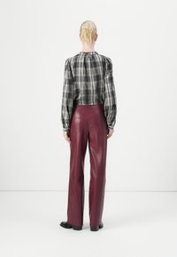 Zwart-wit geblokt blouse met puffmouwen, gecombineerd met bordeauxkleurige, high-waisted neplederen broek en zwarte schoenen.