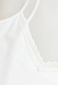 Camisolă albă cu dantelă delicată la decolteu. Confecționată din material moale, cu bretele subțiri reglabile și textură netedă.