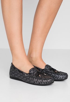 Chaussures plates noires et grises avec un motif texturé arborant les initiales 'MK'. Bout arrondi et détails de laçage à l'avant.