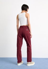 Jeans în nuanță de vișiniu, cu talie înaltă, cu două buzunare pe spate și un eticheta. Asortate cu un top scurt alb și adidași bej cu un model.