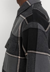 Harmaa ruudullinen flanellipaita, jossa suuret ruudut, nappilistallinen tasku, kaulus sekä mustavalkoiset kontrastiviivat. Pehmeä rakenne.