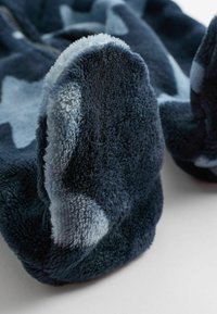 Tummansininen fleece-jalkine, pehmeällä, teksturoidulla kankaalla, jossa on vaaleansinisiä tähtikuvioita ja pyöreät, pehmeät pohjat.