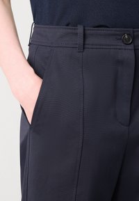 Námořnické modré kalhoty s hladkým povrchem, postranními kapsami, poutky na opasek a knoflíkovým zapínáním, s úhlednými prošitými detaily.