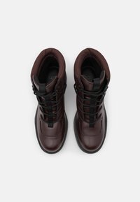 Bottes chelsea en cuir marron avec des lacets noirs, col rembourré et doublure en tissu texturé, doté d'un bout rond et de semelles noires robustes.