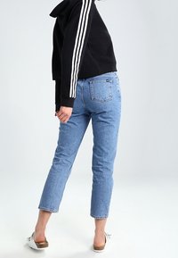 Blue denim jeans with a straight-cut and cropped length, paired with a black hooded sweatshirt featuring white stripes on the sleeves.