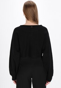 Zwarte cropped trui met lange mouwen, met een wijde halslijn en een kleine metallic accent aan de achterkant. Soepele brei-textuur.