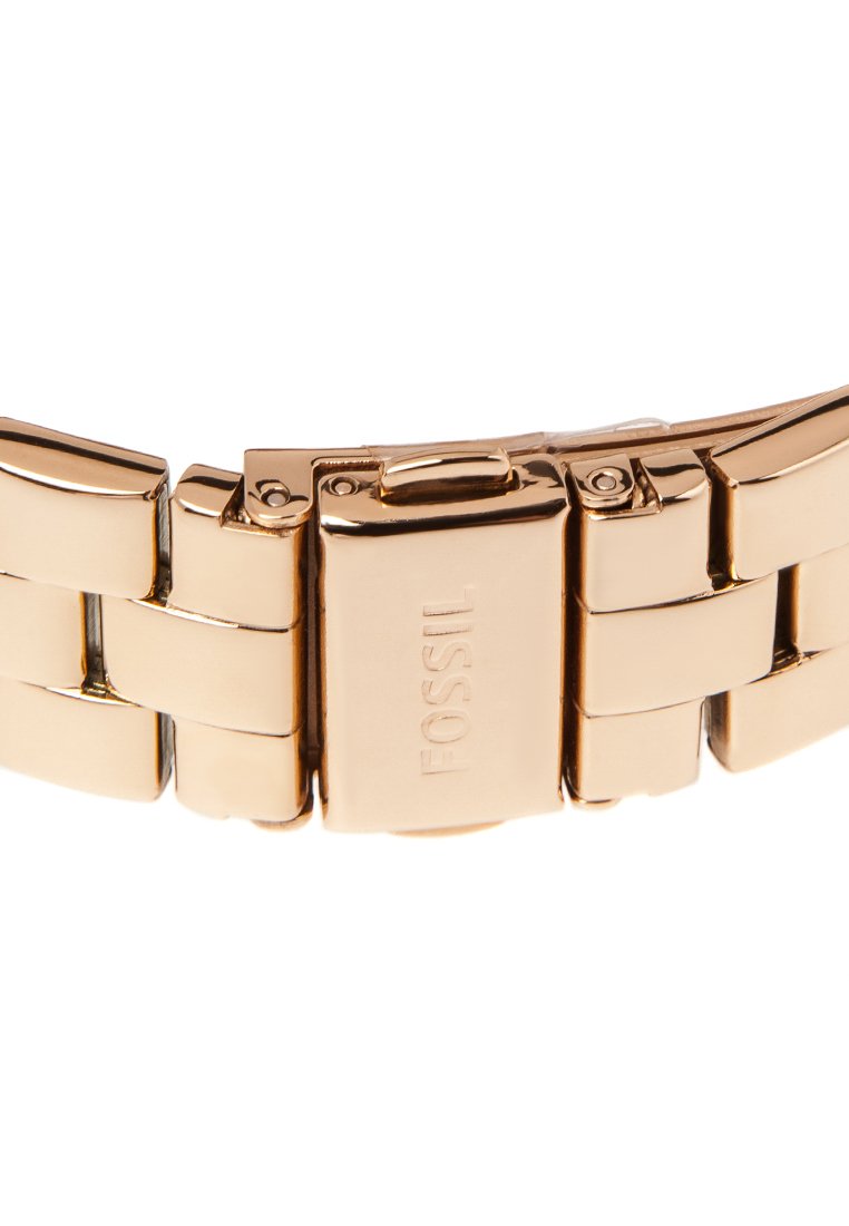 Fermoir en métal doré pour bracelet de montre avec le logo "Fossil" gravé, présentant un mécanisme de verrouillage à bouton-poussoir sécurisé et des segments de bracelet liés.