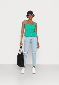 Top peplum floral verde com decote quadrado, combinado com jeans claros rasgados azuis. Chapéu de balde preto, óculos de sol e ténis brancos completam o look.