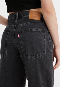 Zwarte denim jeans met hoge taille, voorzien van een leren label aan de achterkant, achterzakken en contrasterende stikseldetails.