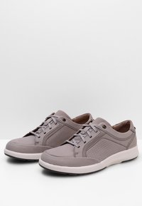 Baskets gris clair en cuir avec des détails perforés, semelle en caoutchouc plate et lacets ronds. Design minimaliste avec une texture douce.