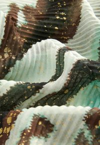Lightweight, patterned fabric with a mix of teal, brown, and gold specks. Features a wavy texture and subtle pleating details.
