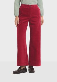 Red corduroy wide-leg trousers with a smooth texture, featuring a front button closure and a high waist. Paired with dark loafers.