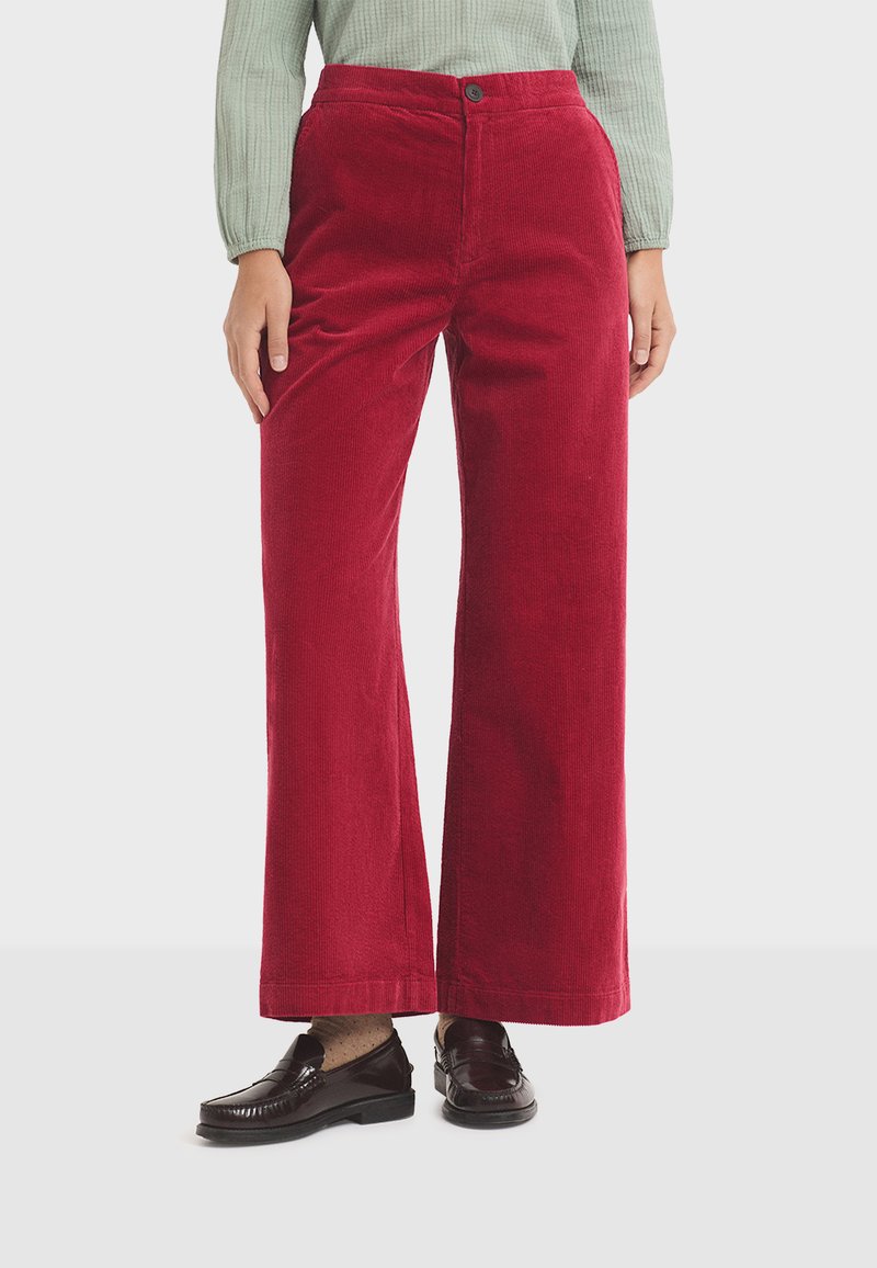 Red corduroy wide-leg trousers with a smooth texture, featuring a front button closure and a high waist. Paired with dark loafers.