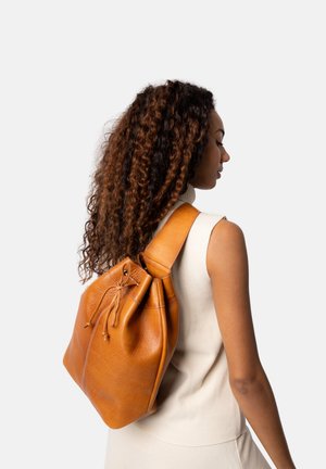 Sac à dos en cuir marron à la conception décontractée, fermeture à cordon et bandoulière réglable. Texture lisse et forme arrondie ; style minimaliste.