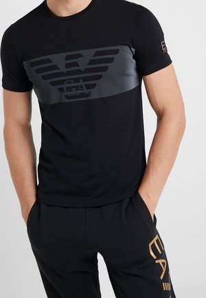 T-shirt en coton noir avec un motif graphique gris, rayures et un emblème. La coupe ajustée présente des manches courtes et un col rond.