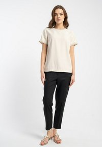 Kremowy krótki top z ozdobnym wykończeniem, w zestawieniu z czarnymi eleganckimi spodniami i jasnymi sandałami, na białym tle.