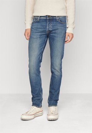 Blauwe denim jeans met een slim fit, met een klassieke vijfzakkenontwerp en subtiele vervaging. Gepaard met witte high-top sneakers.