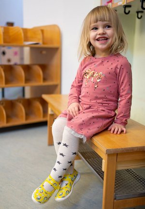 Rosa langärmliges Kleid mit goldenen Sternakzenten, weiße knielange Socken mit schwarzen Sternen und gelbe Schuhe mit einem Cartoon-Design.