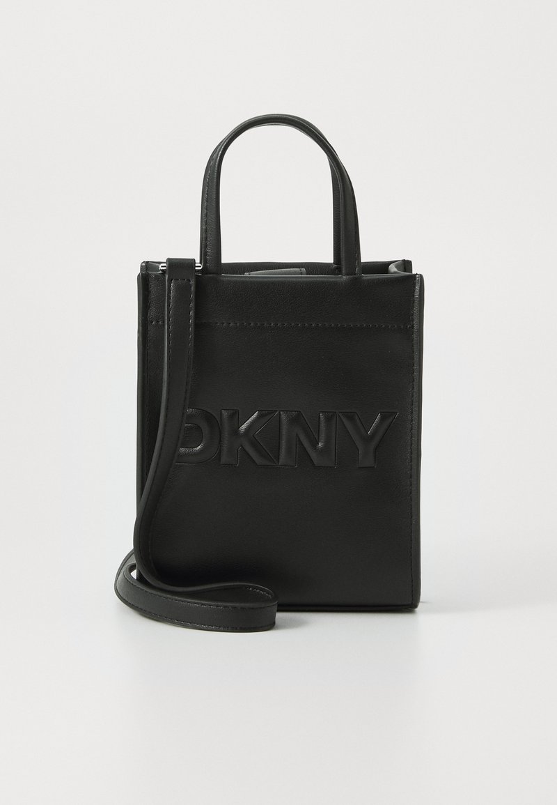 Sac à main rectangulaire en cuir noir avec logo DKNY embossé, doubles poignées et longue bandoulière amovible sur fond uni.