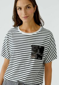Gestreiftes Kurzarm-T-Shirt aus weißer und schwarzer Baumwolle mit einer schwarzen Pailletten-Tasche. Legere Passform, runder Ausschnitt und weiche Textur.