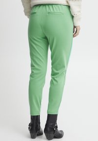 Grüne, anliegende Jogginghosen mit einem elastischen Bund. Mit zwei Gesäßtaschen, glatter Textur und kontrastierendem, hellblauem Seitenstreifen.