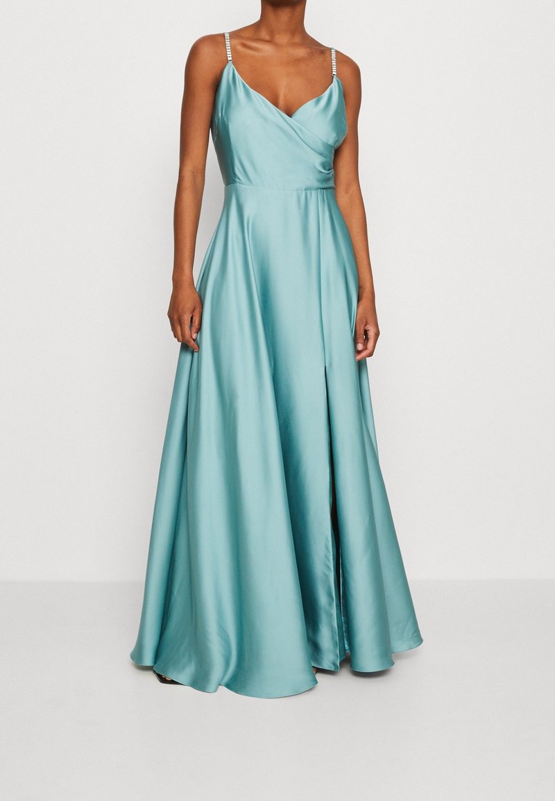 Femme portant une robe longue en satin turquoise avec un corsage portefeuille et de fines bretelles ornées.