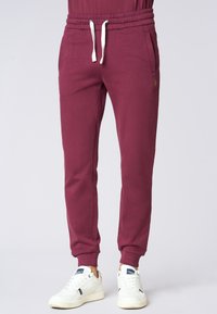 Pantaloni jogger bordeaux realizzati in tessuto morbido, con vita elasticizzata e cordini, tasche laterali e polsini affusolati.