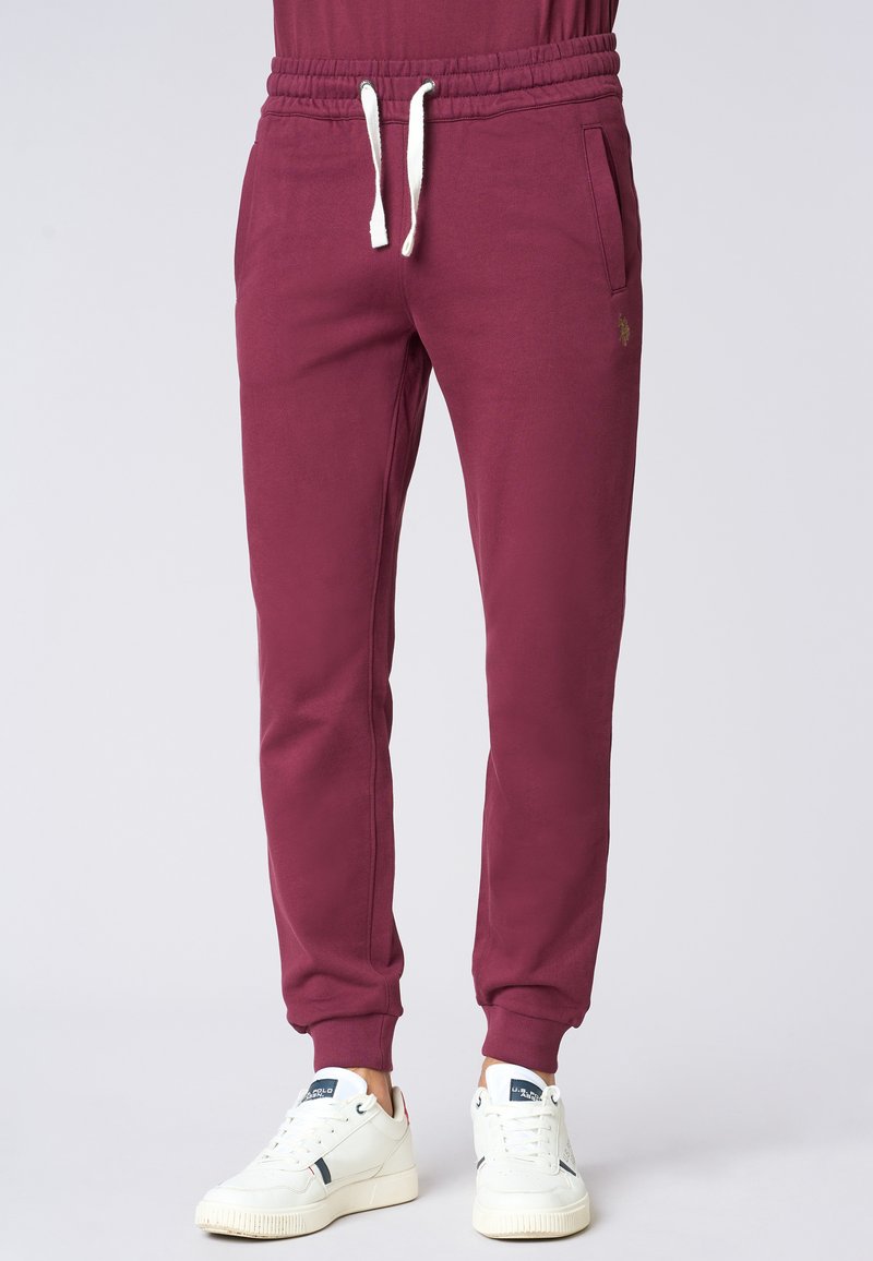Pantaloni jogger bordeaux realizzati in tessuto morbido, con vita elasticizzata e cordini, tasche laterali e polsini affusolati.